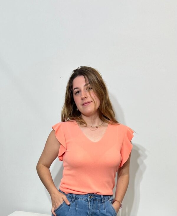 Mujer posando con blusa coral de manga corta con volantes y pantalón vaquero. Compra en Arezzo para descubrir moda femenina única y estilosa.